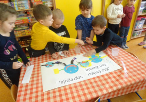 Piątka dzieci dekoruje plakat ekologiczny, naklejają elementy z kolorowego papieru.